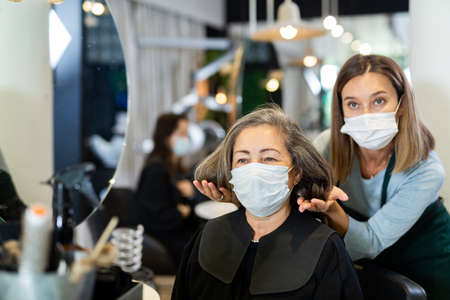 Elderly woman in protective mask sitting in chair of hairstylistの写真素材