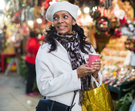 Happy woman holding cup of coffee in hands at street christmas fairの写真素材