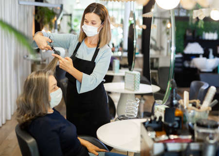 Elderly female client in protective mask getting haircut in hair salonの写真素材