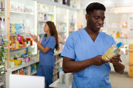 Focused african american male pharmacist is studying the composition of a hair care productの写真素材
