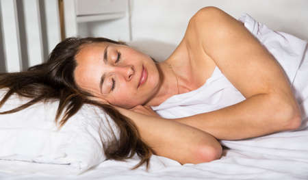 Portrait of relaxed adult woman sleeping in bed alone in homeの写真素材