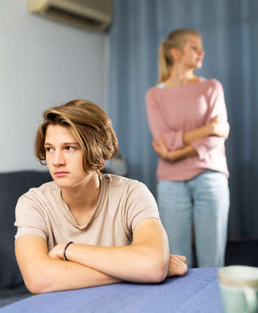 Disappointed teenager sitting at table at home after discord with motherの写真素材