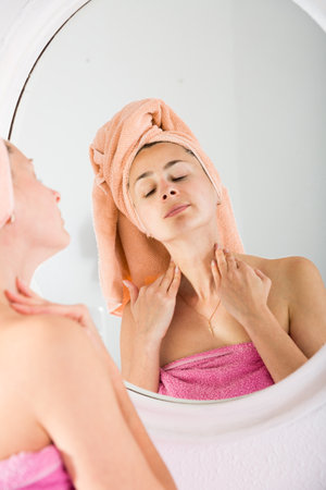 Adult woman with a towel on her head looks in the mirrorの写真素材