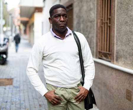 Portrait of african american man in light clothes walking along city streetの写真素材