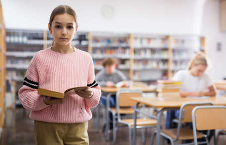 Preteen girl standing alone near bookcase in libraryの写真素材