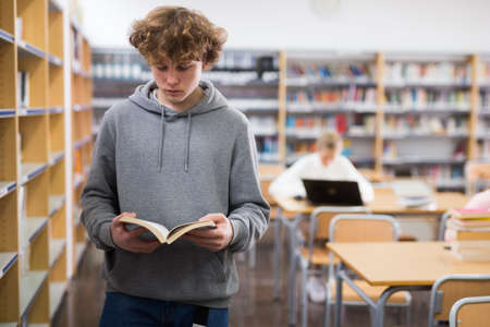 Teenager boy reading book in libraryの写真素材