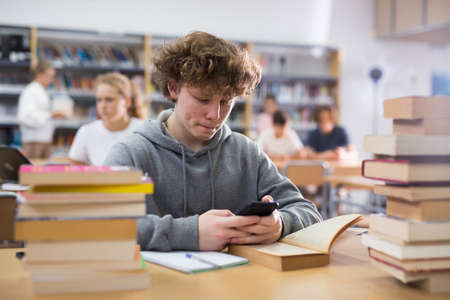 Teenage boy with smartphone in libraryの写真素材