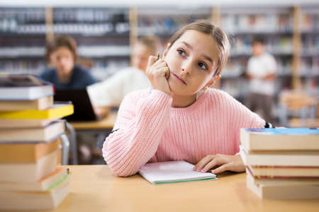 Thoughtful young girl in libraryの写真素材