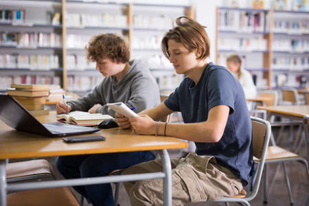 Two teenage friends are reading books and preparing for exams in school libraryの写真素材