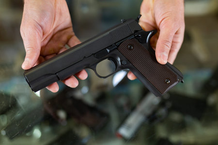 Gunsmith shop assistant demonstrates black pistol in hands