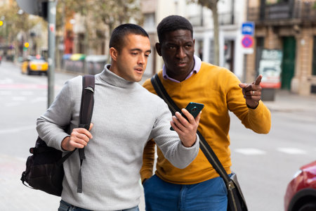 Male tourists with bags are walking down the street. He points forward with hand.