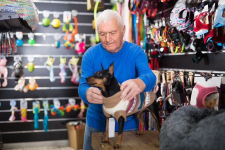 Elderly retired man dressing his dog in winter clothes at pet shop