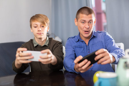 Father and son together playing on their smartphones while sitting at table at home