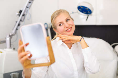 Smiling woman looking in mirror after hardware facial procedureの写真素材