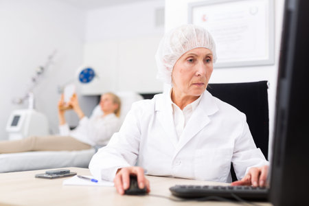 Experienced female cosmetologist working with laptop in aesthetic medicine office