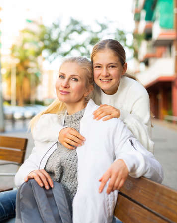 Cheerful teen girl and her mother embracing on city streetの写真素材