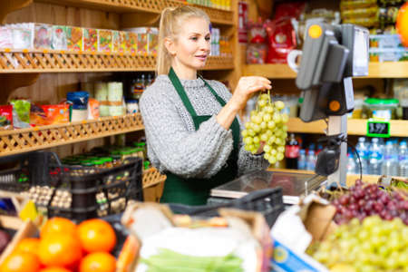 Portrait of a positive female salesperson at the checkout counter at grocery supermarketの写真素材