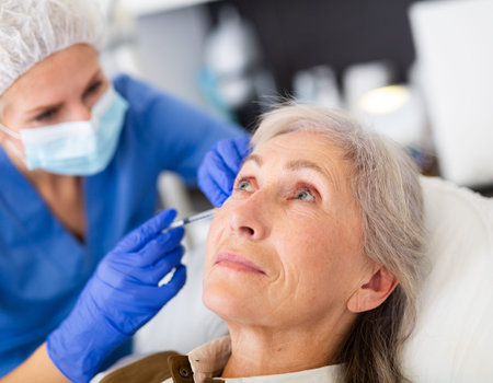 Elderly wman receiving procedure of face mesotherapy at cosmetology clinic