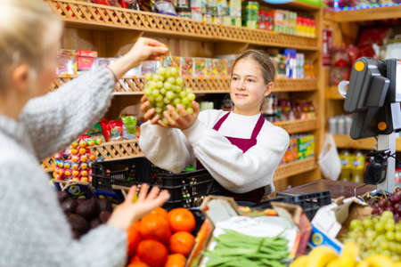 Young salesgirl taking grape from female customer for weighingの写真素材