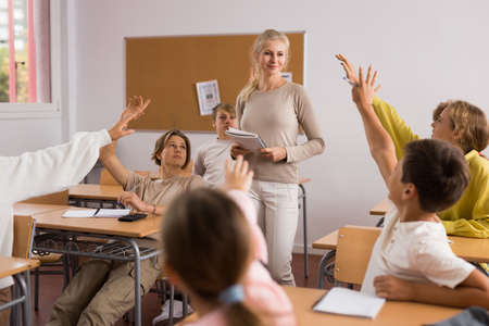School pupils raise their hands up in classroomの写真素材