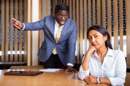 Saddened businesswoman sitting in office with dissatisfied male colleagueの写真素材