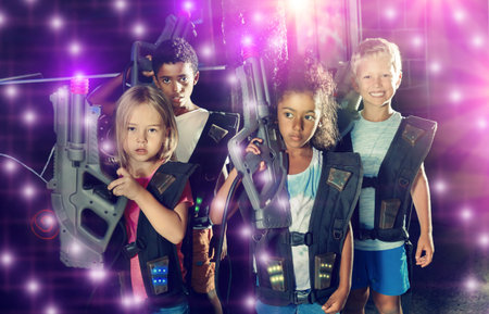 Cheerful teen girl and boys with laser pistols posing together in dark laser tag labyrinthの写真素材