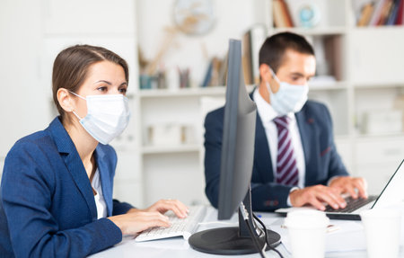 Business woman in face mask working with male colleague in office