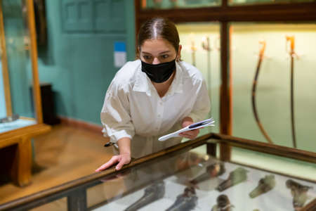 Young female in mask looking at the exposition of mediaeval weaponの写真素材