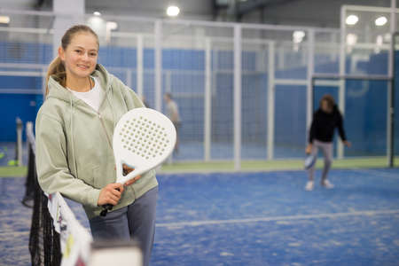 Positive teenage girl looking at camera while playing padel at courtの写真素材