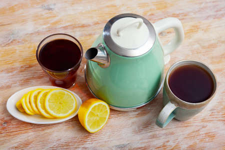 Electric kettle, two cups of tea and sliced lemonの写真素材