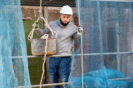 Worker lowering down bucket with construction mortar