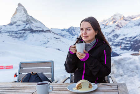 Smiling woman enjoying mulled wine with strudel in outdoor cafe of ski resortの写真素材