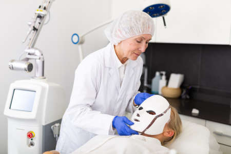 Cosmetologist putting spectrum mask on young womans faceの写真素材
