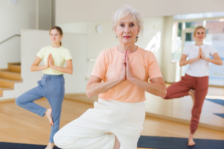 Aged woman standing in tree pose during group yoga trainingの写真素材