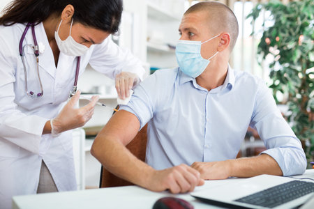 Doctor in mask giving vaccine to pacient in office