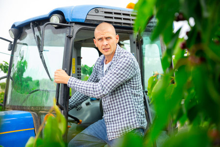 Skilled male farmer working on farm tractor in orchard