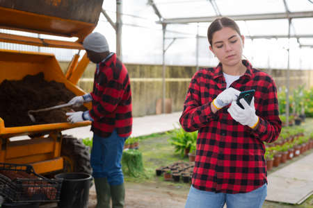 Female gardener standing at greenhouse with smartphoneの写真素材