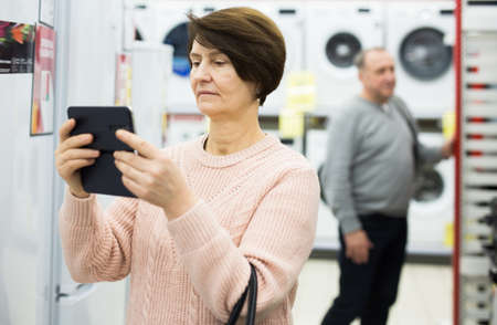 Mature woman photographing with her smartphone in appliance storeの写真素材
