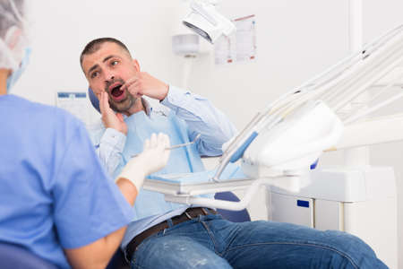 Unhappy american man in medical chair complains of toothacheの写真素材