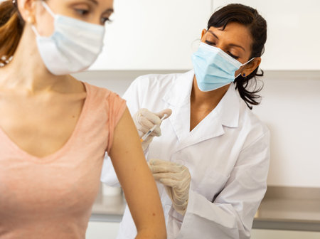 Woman doctor in face mask vaccinating patient