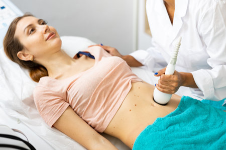 Cosmetologist making ultrasound lifting procedure in abdominal zones