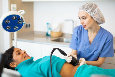 Cosmetologist performing ultrasound cavitation body procedure for client
