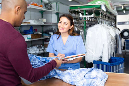 Woman dry-cleaning worker receiving clothes from clientの写真素材