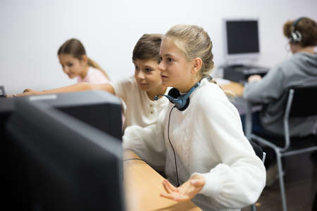 Boy helping upset girl to solve problem on computer in schoolclassの写真素材