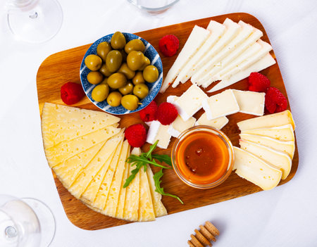 Plate with different types of cheese, raspberries and olives