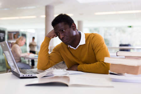 Tired african-american male preparing for exam in university libraryの写真素材