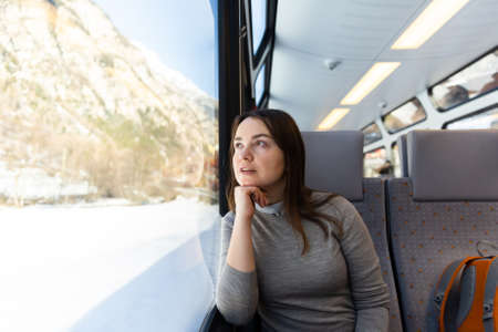Dreamy female traveler admiring Swiss mountain landscapes through train windowの写真素材