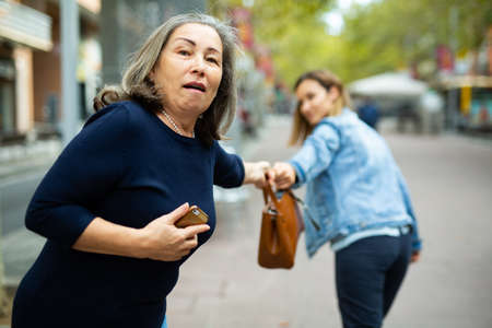 Street thief trying to steal handbag of scared elderly womanの写真素材