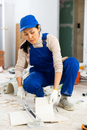 Woman builder cuts ceramic tiles with tile cutterの写真素材