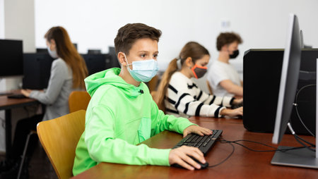 Positive male student wearing face mask working on computer in library. Concept of adult self...